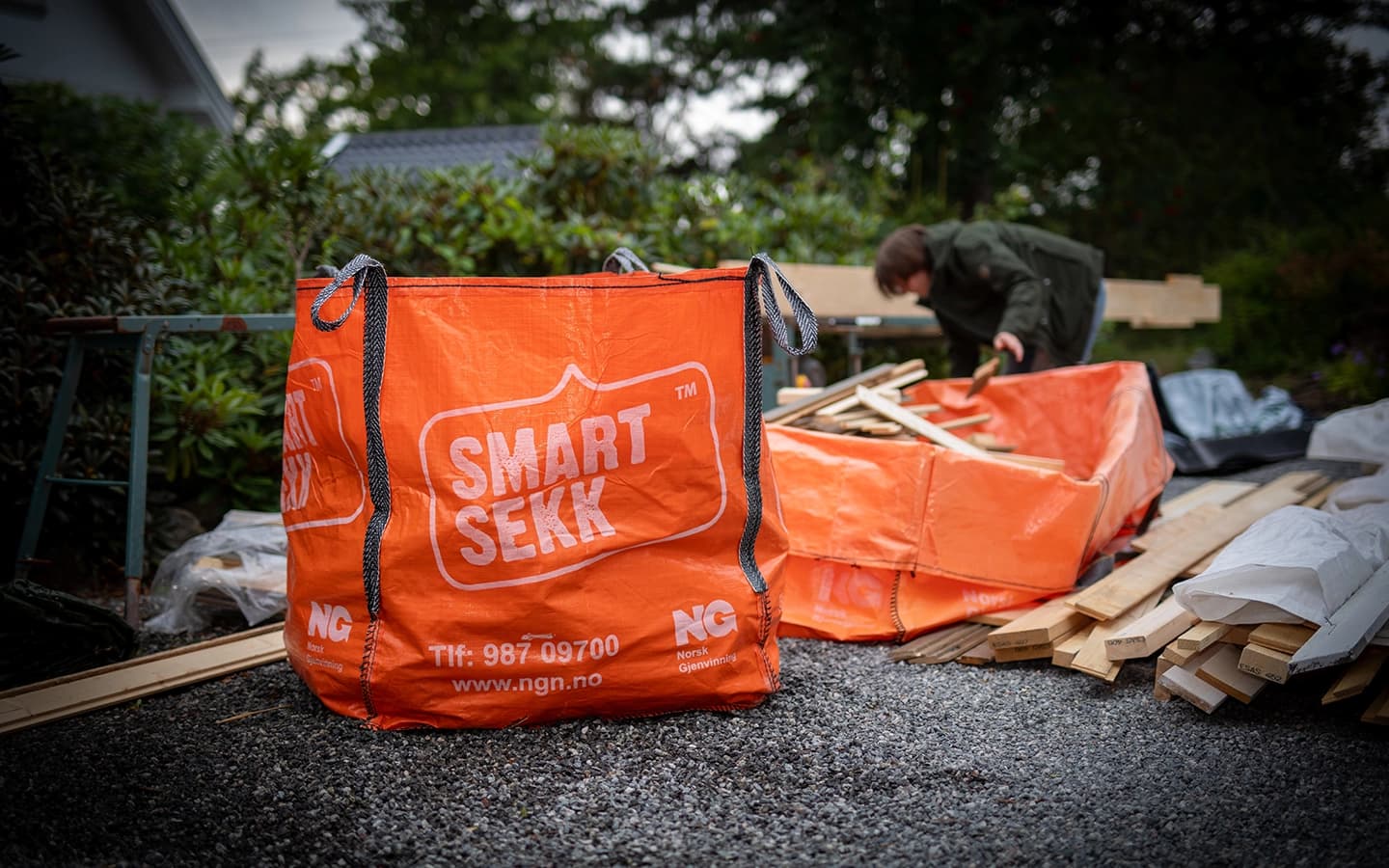 Mann kaster treverk i en oransje sekk for avfall. Foto.